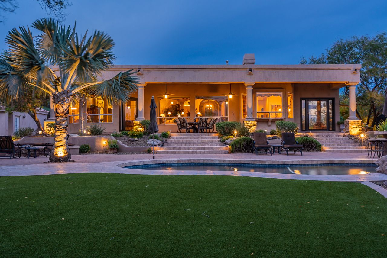 Covered patio and pool of an Arizona home at twilight, with warm lights glowing through the windows