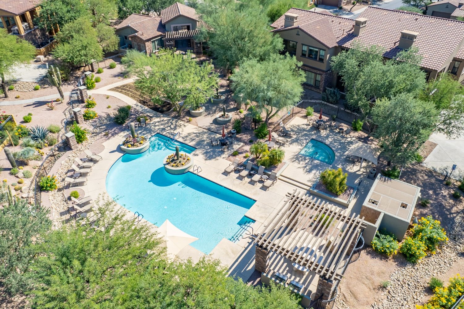 Aerial view of an Arizona community pool and spa surrounded by lounge chairs, shade trees, desert landscaping and nearby homes