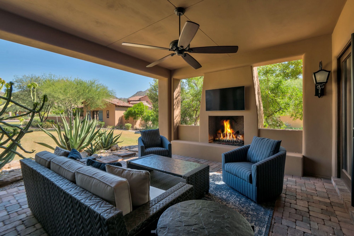 Covered Arizona patio with an outdoor fireplace, wicker sofa and swivel chairs overlooking desert landscaping and mountains