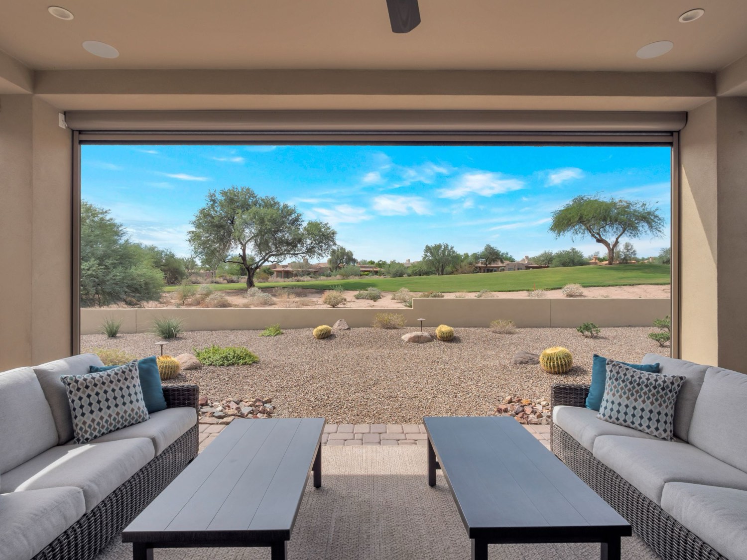 Covered patio of an Arizona home with outdoor sofas looking out over desert landscaping to a golf course fairway and blue sky
