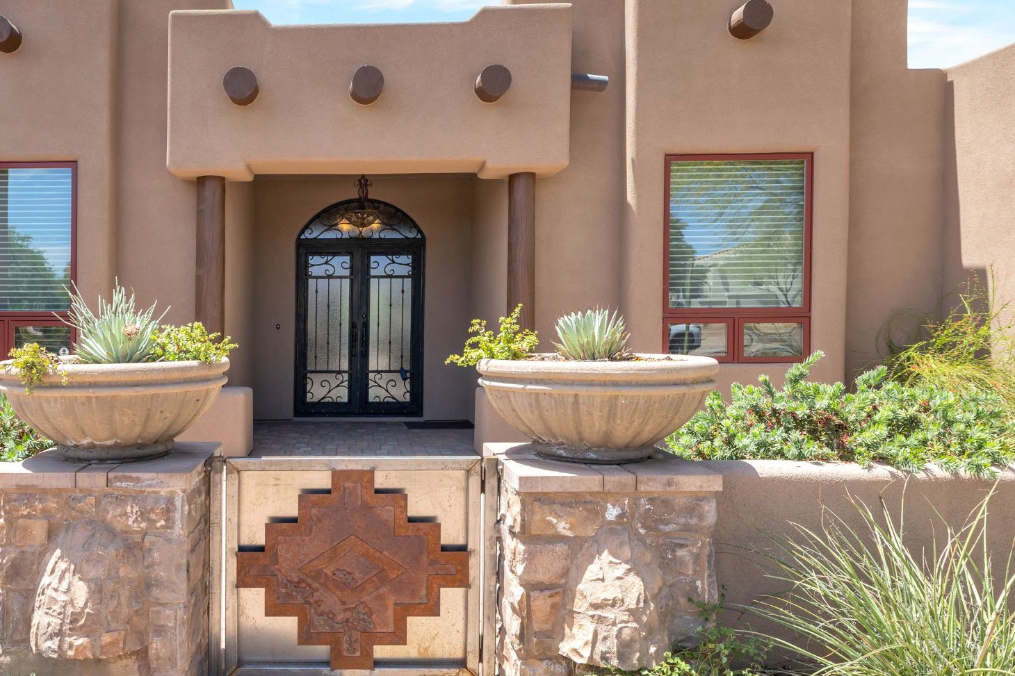 Southwest-style Arizona home with an arched iron front door, stone pillars, a decorative gate and desert plantings